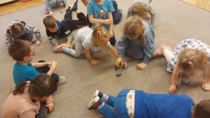 grupa dzieci bawi sie na dywanie niebieskimi piórkami