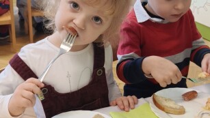 dziewczynka spożywa posiłek, w tle dzieci siedza przy nakrytym stole