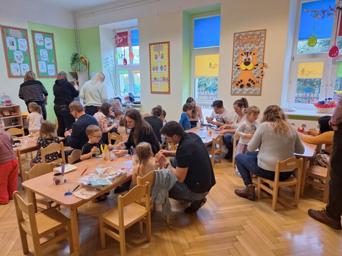 widok sali przedszkolnej w której rodzic ei dzieci przygotowują przy stolikach dekoracje wielkanocne