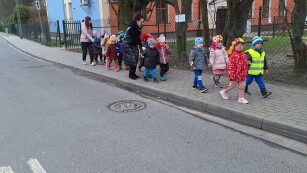 dzieci z paniami idą w rzędzie chodnikiem pani pochyla się nad dziećmi