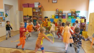 grupa dzieci bawi się na sali, dzieci ubrane w tonacji pomarańczowej
