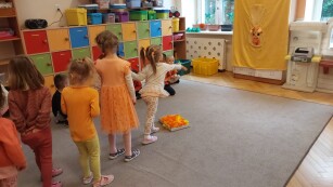 grupa dzieci bawi się na sali, dzieci ubrane w tonacji pomarańczowej, rzucają do celu