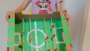 na zdjęciu dziewczynka pozuje do zdjęcia z eko zabawką, trzyma w rękach piłkarzyki