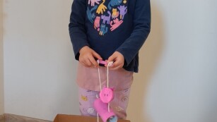 dziewczynka pozuje na zdjęciu z eko zabawką, w pudełku jest gra kółko i krzyżyk oraz świnka na sznureczkach