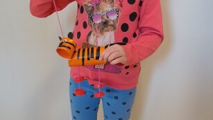dziewczynka pozuje na zdjęciu z eko zabawką, trzyma w ręku tygryska na sznureczkach