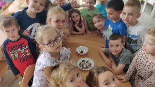 Dzieci stoją przy stoliku na którym jest miseczka z czekoladą