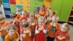 dzieci piją sok pomarańczowy, w większkości ubrane w kolory w odcieniach pomaranczu