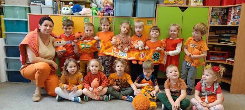 grupa dzieci z panią pozują do zdjęcia, większość ubrana w kolorach pomarańczu