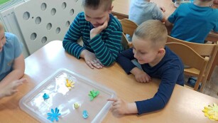 Chłopcy przy stoliku oglądają jak rozwijają się kwiaty z papieru