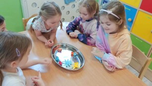 Dziewczynki przy stoliku oglądają jak rozwijają się kwiaty z papieru