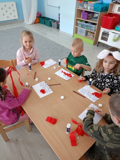 Dzieci przy stoliku wyklejają flagę z białych i czerwonych kulek papieru