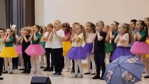 grupa dzieci występuje na scenie w kolorowych ubraniach dzieci zakrywają usta i mają zdziwione miny