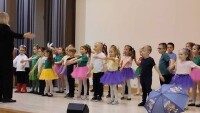 grupa dzieci kolorowo ubranych występuje na scenie śpiewając piosenkę
