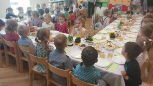 dzieci odświętne ubrane siedzą przy nakrytym duzym stole wielkanocnymi smakołykami