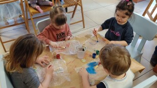 Czwórka dzieci siedzi przy stoliku i maluja farbami