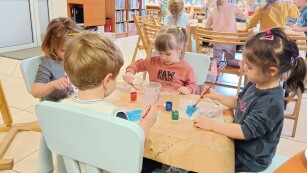 Czwórka dzieci siedzi przy małym stoliku i maluja farbami