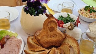 na stole nakrytym obrusem znajdują się dekoracje wielkanocne, w cenrtum babka w krztałcie kurczaka