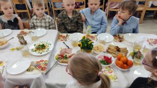 Dzieci siedzą przy odświętnie przygotowanym stole z okazji śniadania wielkanocnego