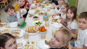Dzieci siedzą przy odświętnie przygotowanym stole z okazji śniadania wielkanocnego