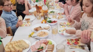 zbliżenie na długi stół z białym obrusem i nakryciami dzieci elegancko ubrane siedzą przy stole czekając na posiłek