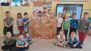 grupa dzieci prezentuje wspólnie narysowany obrazek królów podających sobie ręce  na ścianie monitor ze zdjęciem historycznym podpisania Unii Lubelskiej