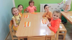 Dzieci siedzą przy stoliku przed sobą mają literki i karty do zabawy