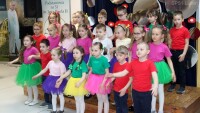 grupa dzieci ubranych na kolorowo śpiewa unosząc ręce