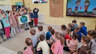 grupa dzieci w sali przedszkolnej połowa stoi tzrymając ekologiczny plakat druga połow asiedzi naprzeciwko i ogląda